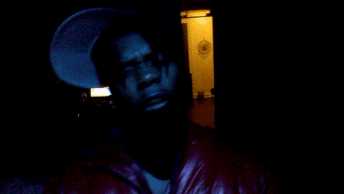 a man in a white hat is making a hand gesture in the dark