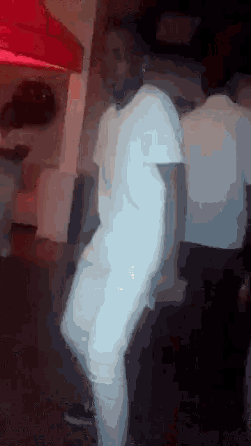 a man in a white shirt is dancing in a room with other people .