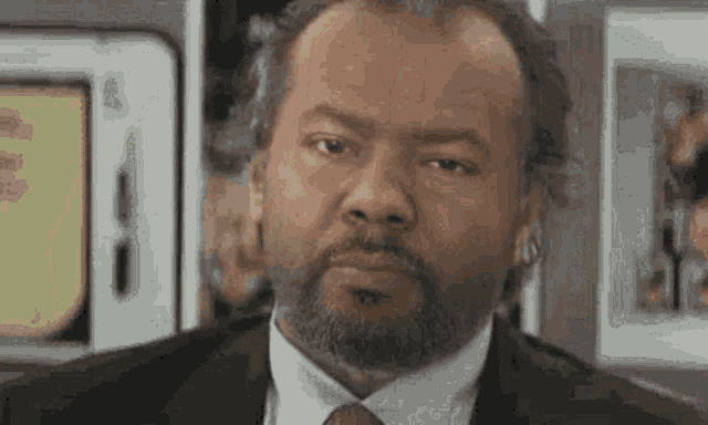 a man with a beard and a suit and tie is looking at the camera .