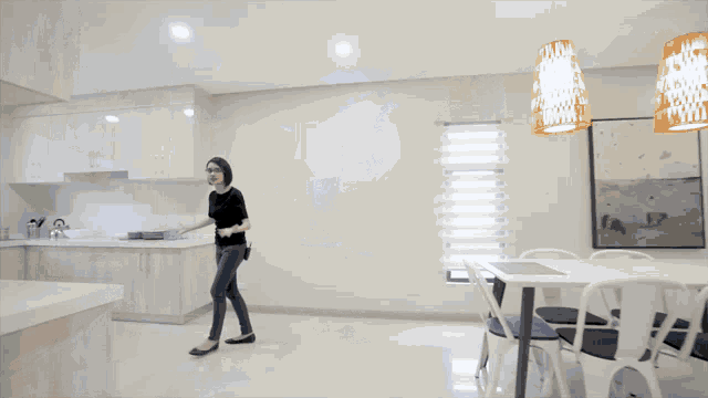 a woman standing in a kitchen with a dining table and chairs