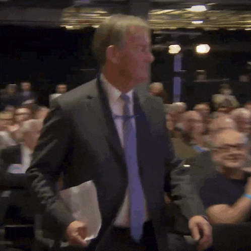 a man in a suit and tie is walking in front of a crowd of people