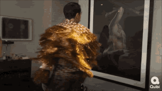 a man in a gold feathered cape is standing in front of a quibi ad