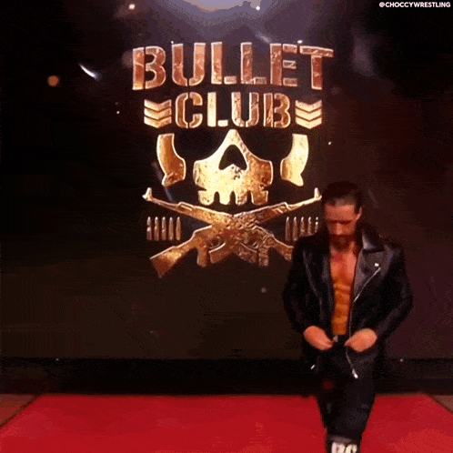 a man in a leather jacket is walking down a red carpet in front of a bullet club logo