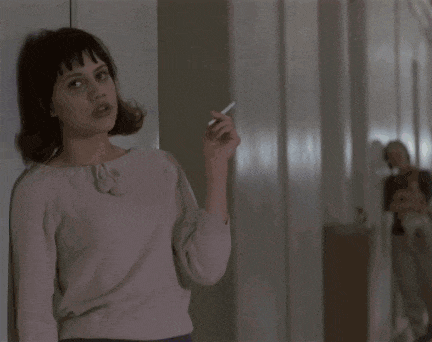a woman smoking a cigarette in a hallway while another woman looks on