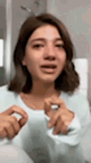 a woman is crying in a bathroom while wearing a white shirt and holding her hands to her face .