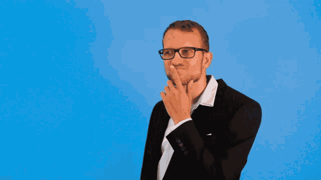 a man wearing glasses and a suit has his finger on his chin