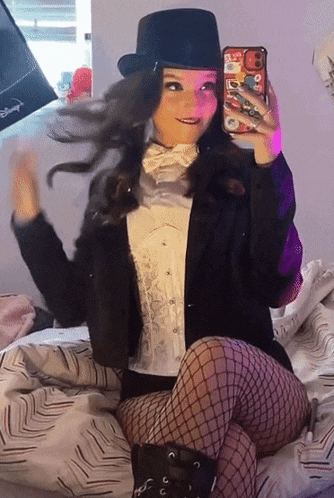 a woman in a tuxedo and top hat is taking a selfie with her phone