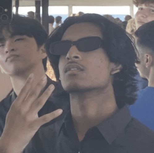 a man wearing sunglasses looks at the camera while another man looks on