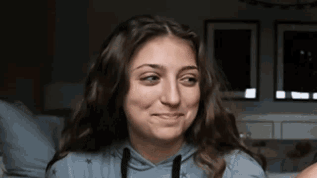 a woman in a blue hoodie is smiling and making a funny face .