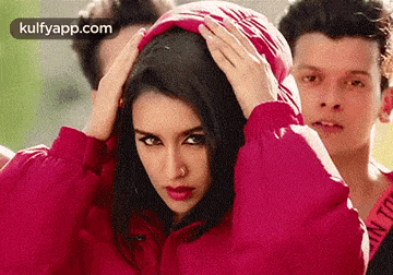 a woman in a red jacket with a hood on her head is standing next to two men .