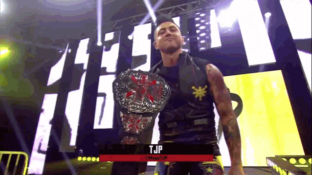 a man holding a wrestling championship belt with the name tjp on the bottom right