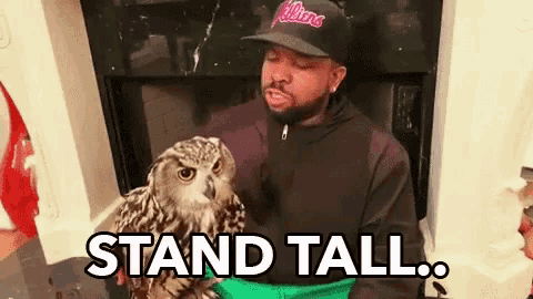 a man in a hat is holding an owl in his arms .