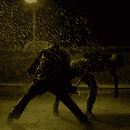 two men are fighting in the rain at night and one of them is wearing boxing gloves