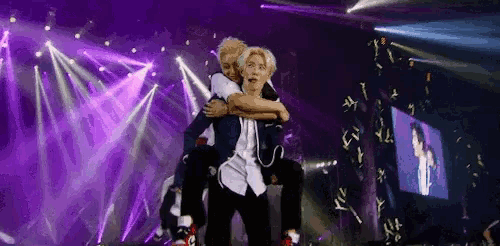 two men are hugging each other on a stage with purple lights behind them .