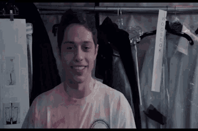 a man wearing a pink tie dye shirt is smiling in front of a hanger with a tag that says wooseok