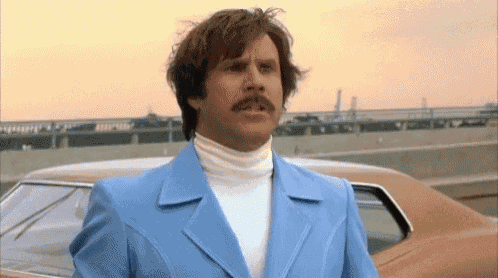 a man with a mustache is wearing a blue suit and standing in front of a car .