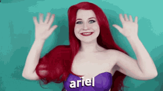 a woman with red hair and a purple top that says ariel on it