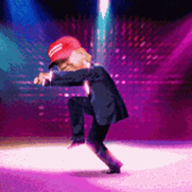 donald trump is dancing on a stage wearing a maga hat