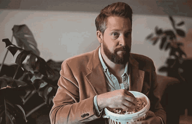 a man in a suit is eating popcorn from a white bucket