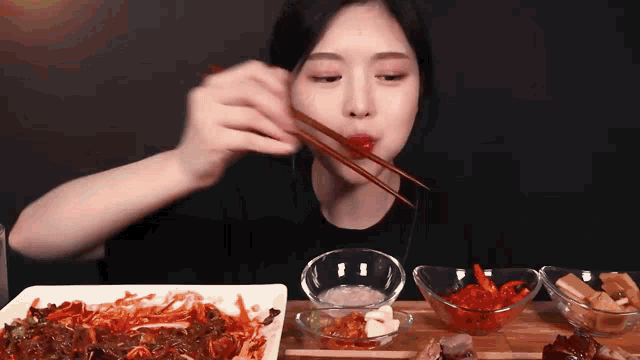 a woman is eating food with chopsticks and a bowl of food in the background