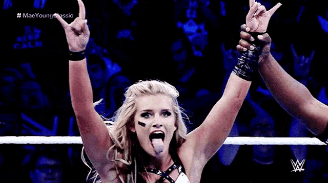 a woman in a wrestling ring with her hands in the air and her tongue hanging out .