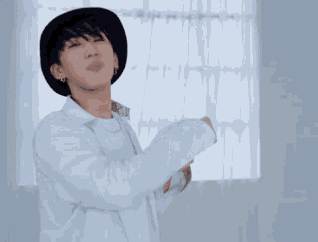 a young man wearing a hat and a white shirt is making a heart with his hands