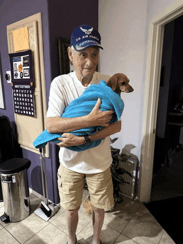a man wearing a u.s. air force hat is holding a small dog wrapped in a blue towel