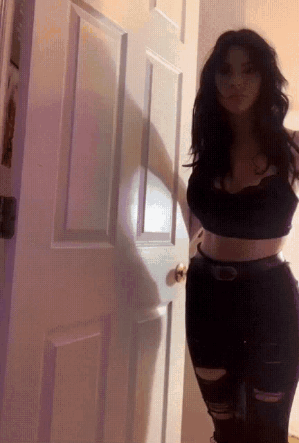 a woman in a black crop top and ripped jeans stands in front of a door
