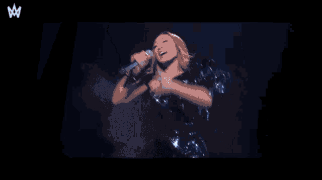 a woman singing into a microphone in front of a crown logo