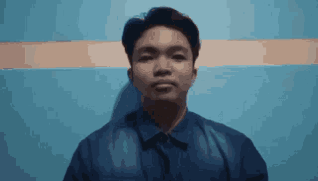 a man in a blue shirt is standing in front of a blue wall and making a funny face .