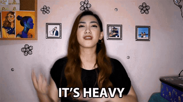 a woman says it 's heavy while standing in front of a wall with pictures on it