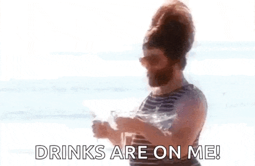 a man with a beard is standing on a beach holding a glass of water and saying `` drinks are on me '' .