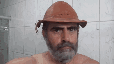a man with a beard and a hat is standing in a bathroom .