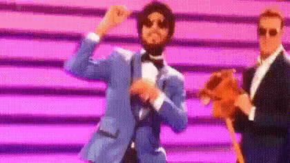 a man in a blue suit and bow tie is dancing on a stage while another man holds a stuffed animal .
