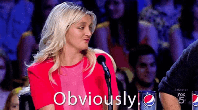 a woman in a red jacket is sitting in front of a microphone with the word obviously written on the screen .