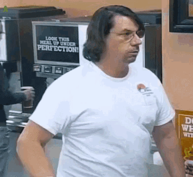 a man in a white t-shirt is standing in front of a machine that says look this meal up under perfection
