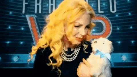a woman with blonde hair is holding a small white dog in front of a sign that says " fratello "