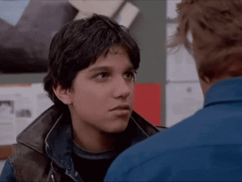 a man in a blue shirt is talking to a young boy in a leather jacket