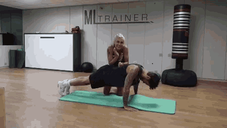 a woman helps a man do push ups on a mat in front of a sign that says mitrainer