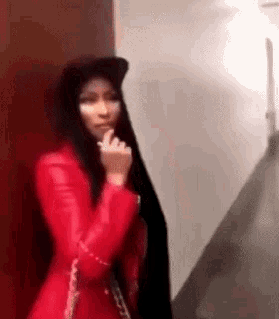 a woman in a red jacket and black hijab is standing in a hallway .