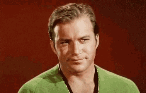a close up of a man wearing a green sweater and smiling against a red background .