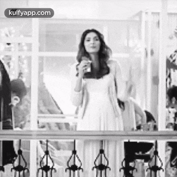 a black and white photo of a woman in a white dress standing on a balcony .