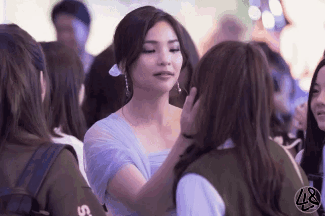 a woman in a purple dress is touching another woman 's face in a crowd of people