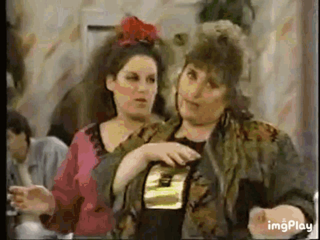 two women are standing next to each other in a room and one of them is holding a bottle .