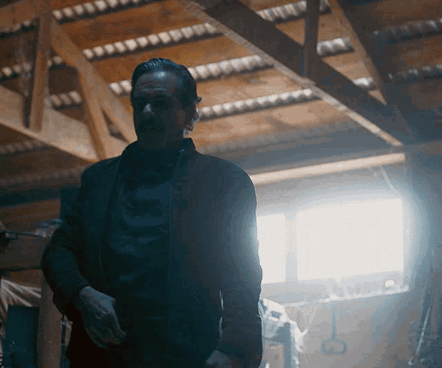a man is standing in a dark room with a light shining through the ceiling