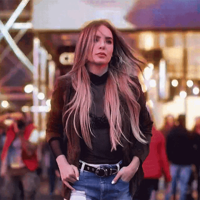 a woman walking down a street with her hands in her pockets wearing a black top