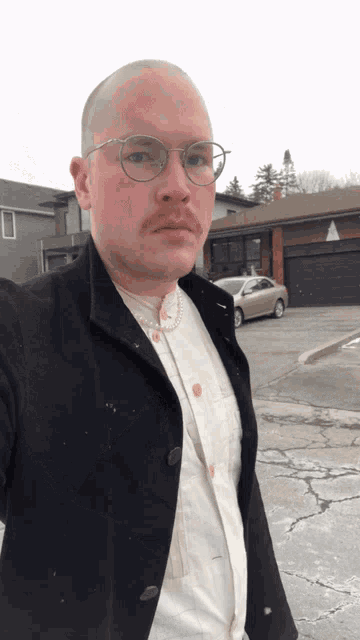a man wearing glasses and a white shirt is standing in front of a garage
