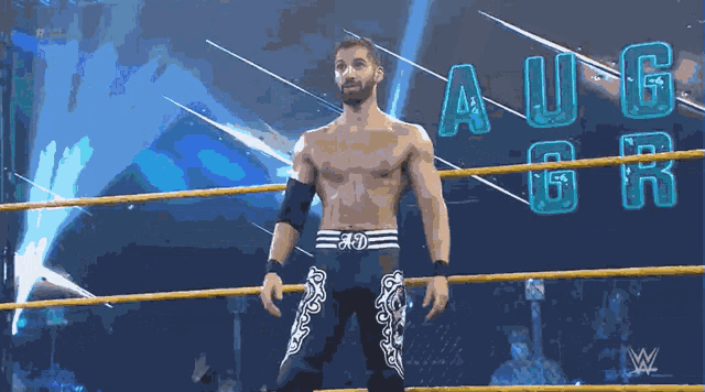 a shirtless wrestler stands in a wrestling ring with the letters aug on the back