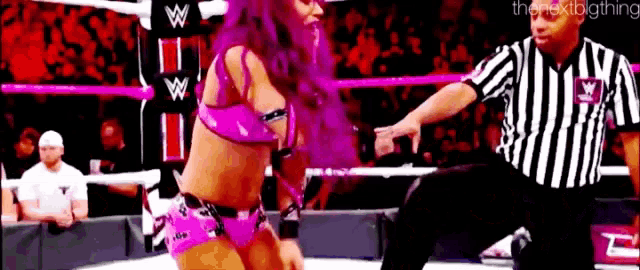 a woman in a pink bikini is dancing in a wrestling ring while a referee looks on .