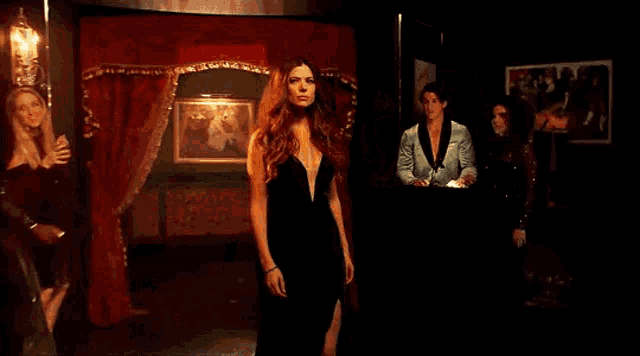 a woman in a black dress is standing in a dark room surrounded by other women .